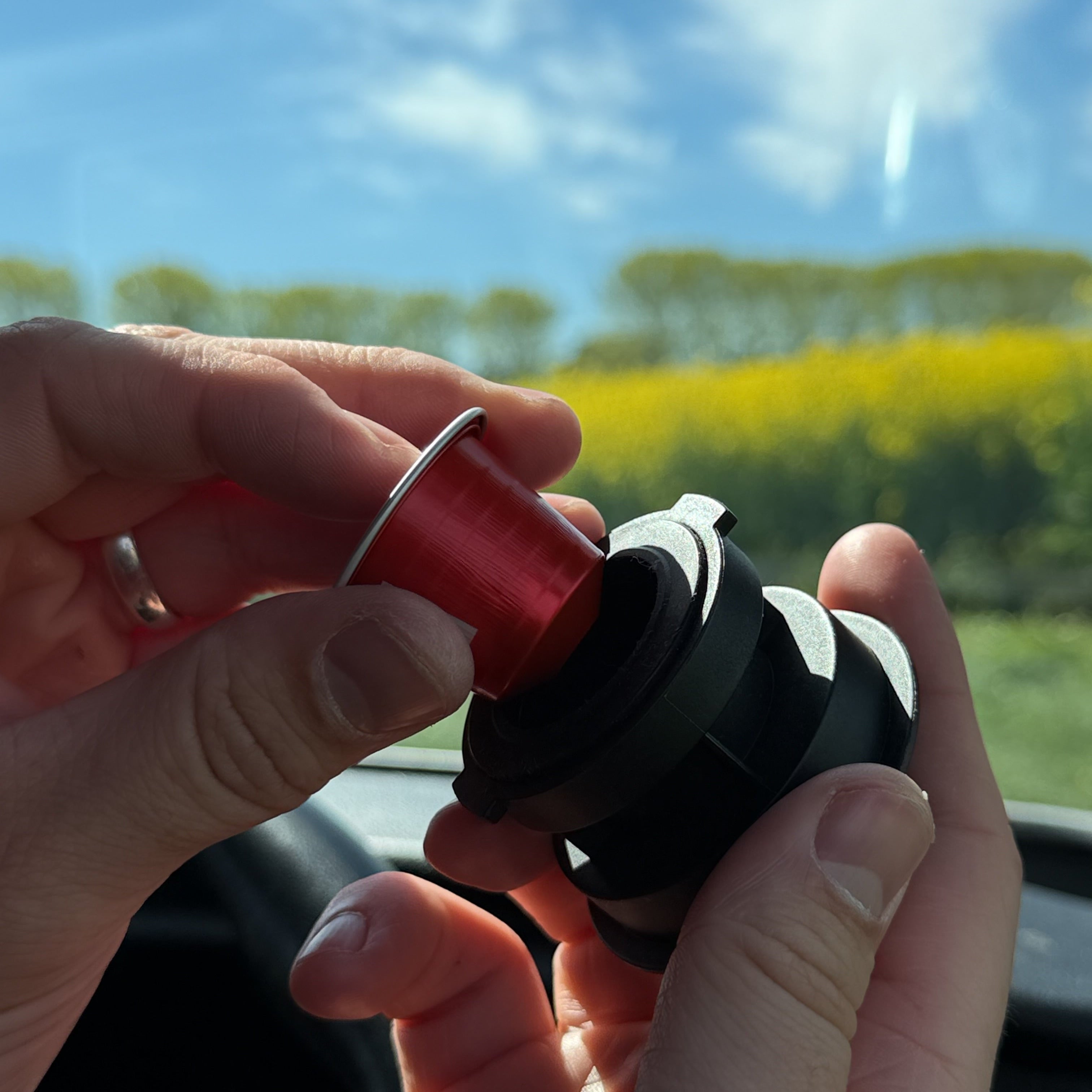 Person holding a red nespresso coffee capsule loading into a portable espresso maker container