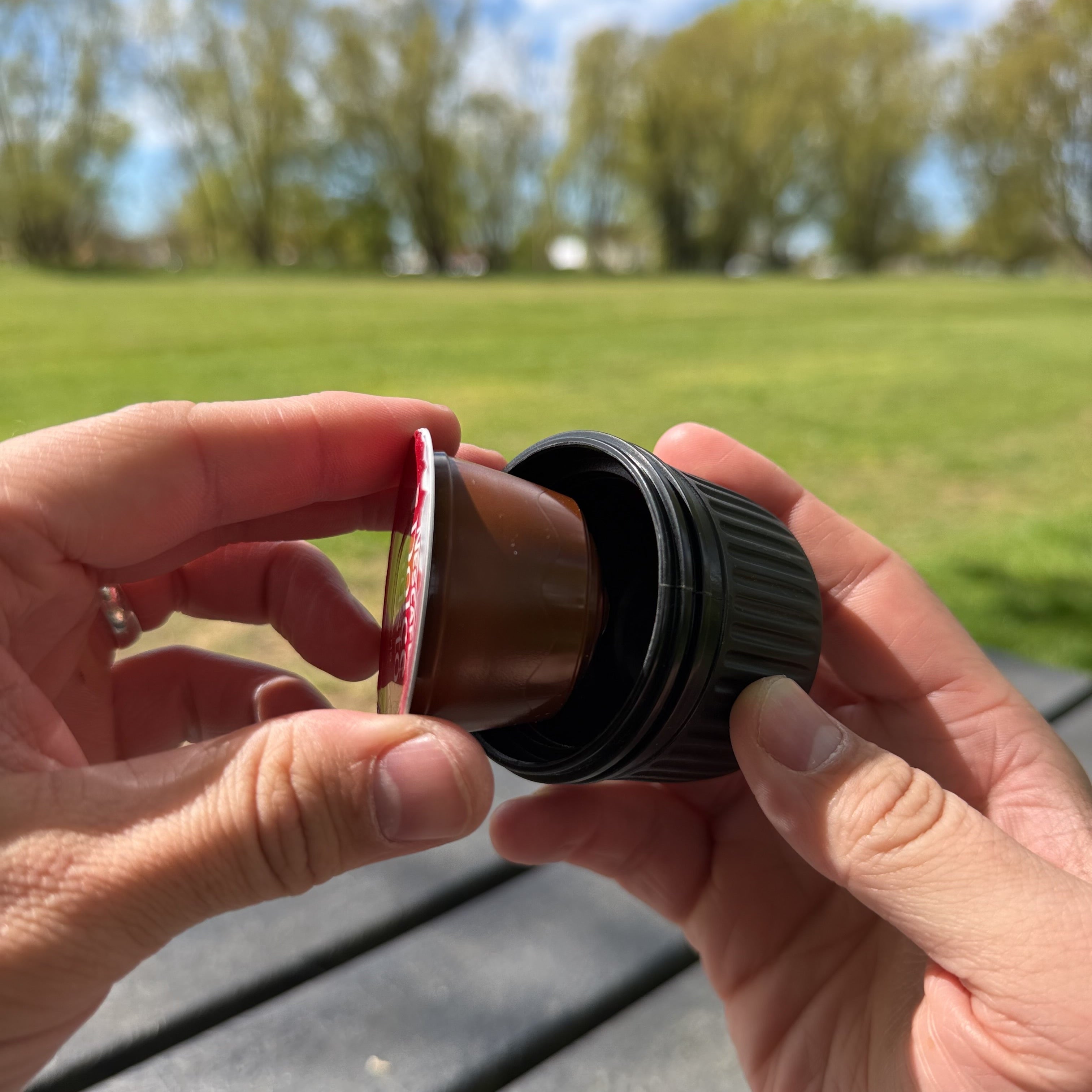 Person holding a dolce gusto coffee pod loading it into a portable espresso maker container