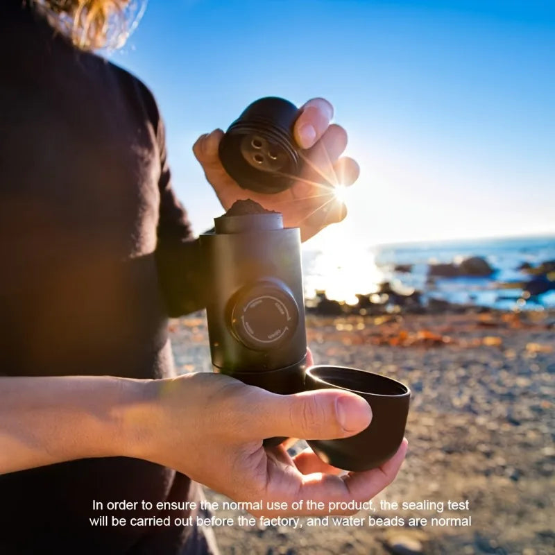 Person using portable coffee maker on a sunny beach, holding coffee grounds and cup
