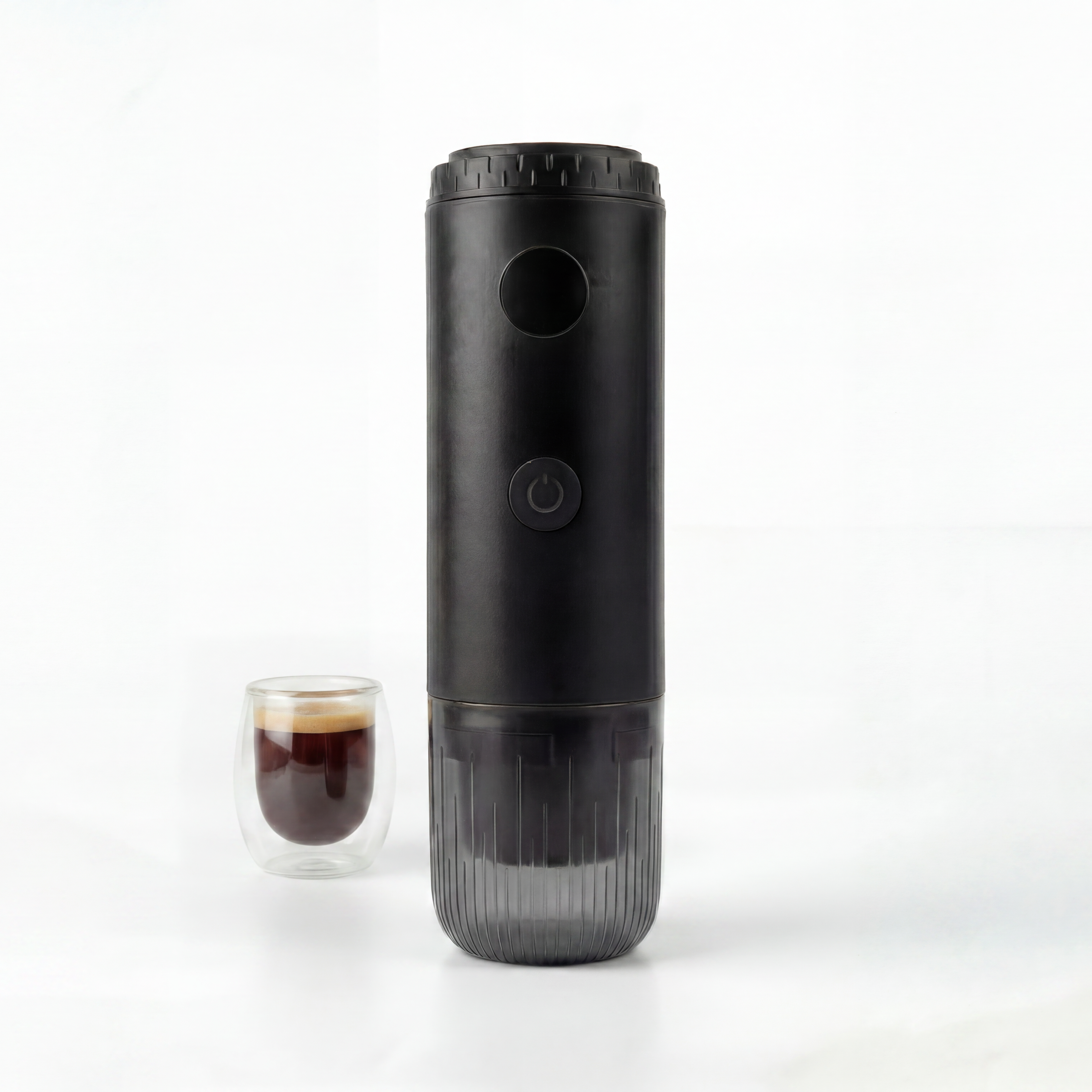 Black portable espresso maker next to a glass of coffee on a white background