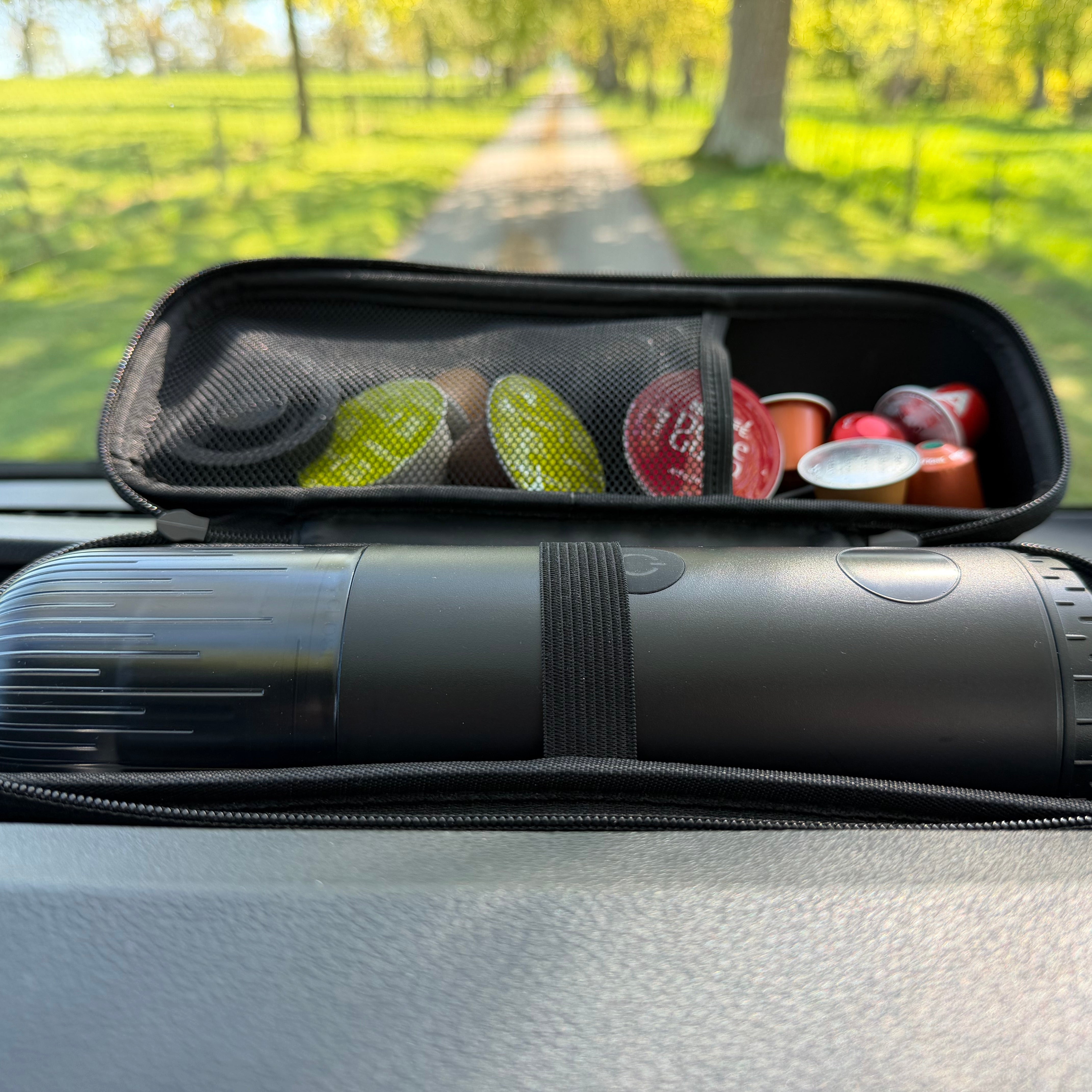 Black portable espresso maker in a carry case within a car with coffee pods in the background