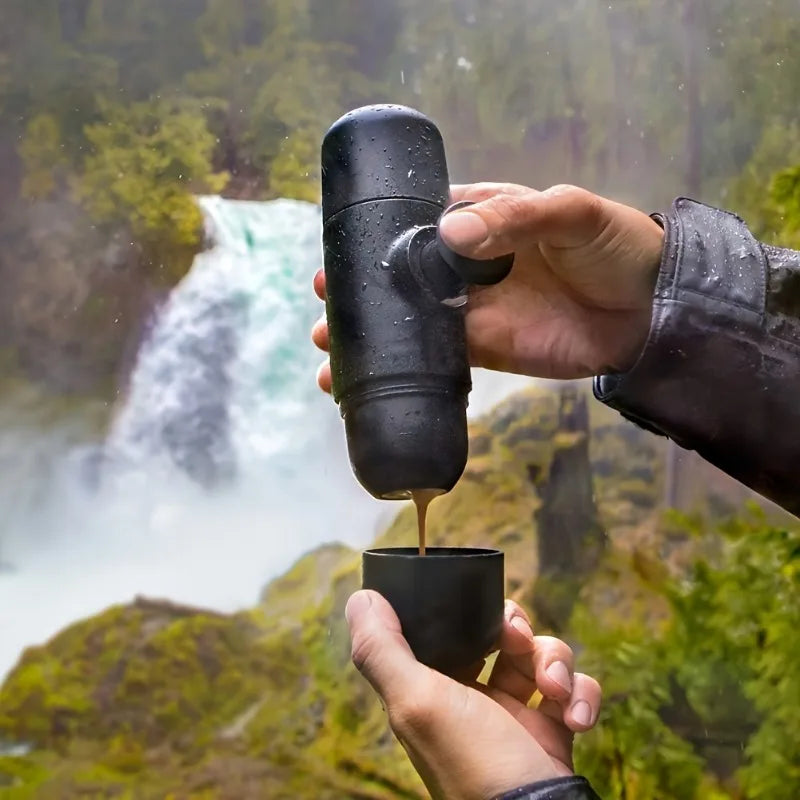 Portable coffee maker dispensing coffee into cup outdoors near waterfall, adventure travel