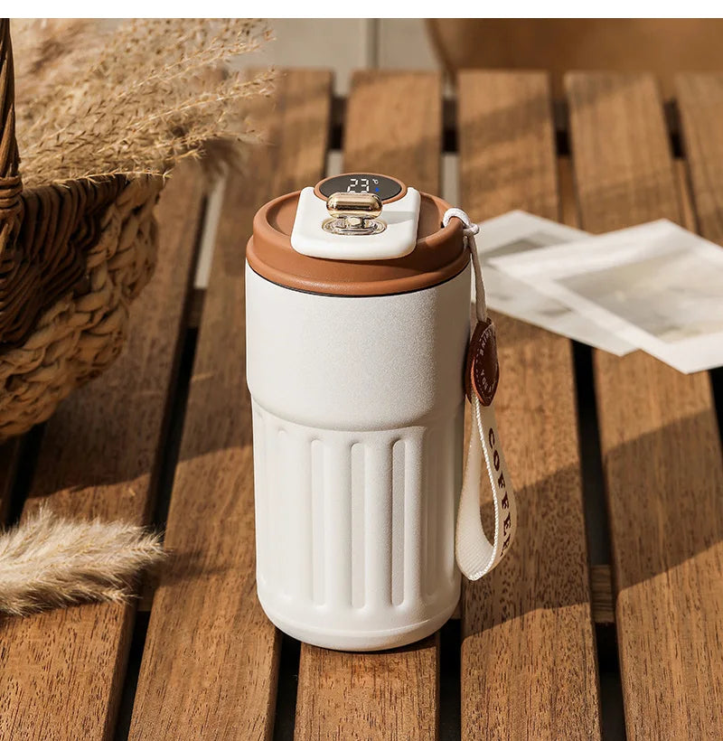Modern insulated coffee tumbler with digital temperature display on wooden table outdoors