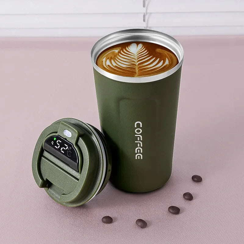 Insulated green travel coffee mug with latte art, digital lid, and scattered coffee beans.
