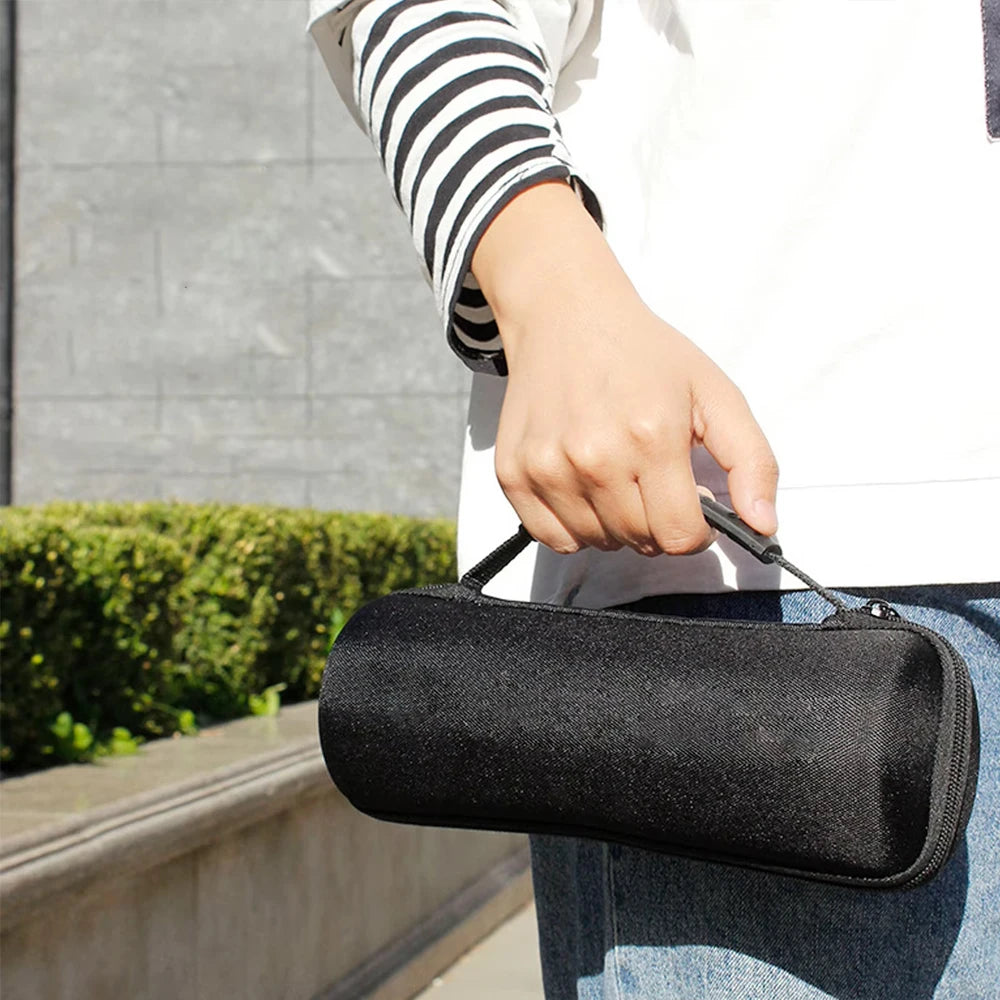 Person holding a black cylindrical carrying case outside, portable accessory bag