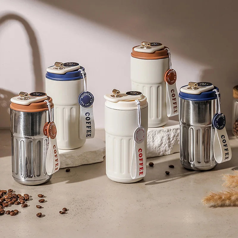 Stylish reusable coffee travel mugs with tags, in white and metallic finishes, on a countertop.