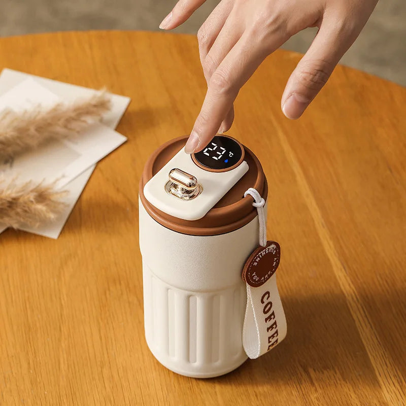 Hand touching smart coffee tumbler with temperature display on wooden table