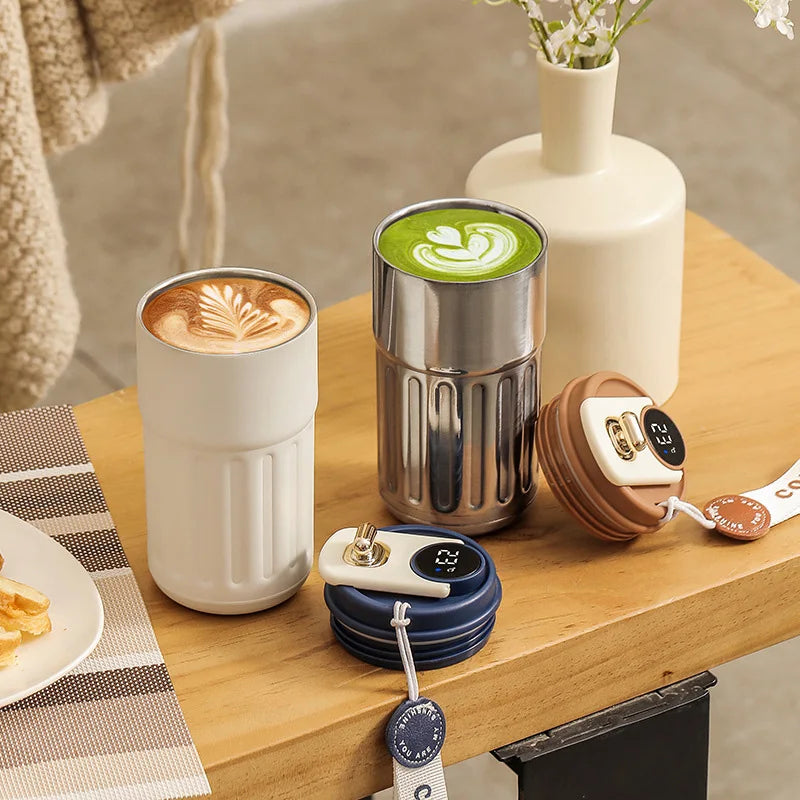Two insulated coffee cups with latte art and matcha on a wooden table, collapsible lids beside them.